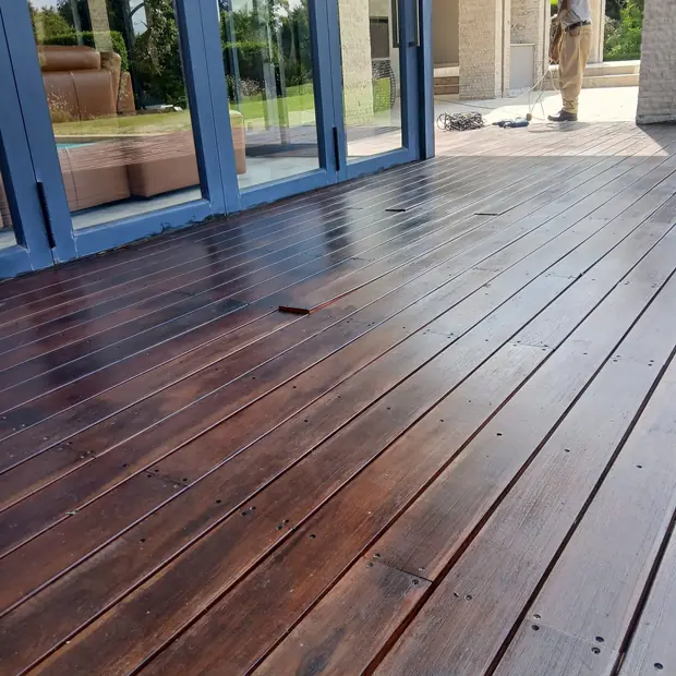Dark oiled timber deck under cover beside folding glass doors in Waterfall, built by Impi Teak